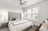 Furnished bedroom with lighted ceiling fan, two windows and bedside tables with lamps