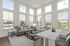 Furnished living area with six windows, grey couches, and a view of a dining table.