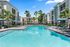Luxurious apartment complex with a sparkling blue pool, palm trees, and cozy lounge chairs under umbrellas, perfect for relaxation and enjoyment.