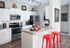 Modern kitchen with sleek white cabinets, stainless steel appliances, and vibrant red bar stools for a stylish touch.