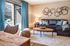 Inviting living room with stylish decor, featuring a cozy sofa, elegant wooden table, and abundant natural light from large windows draped in ocean-blue curtains.