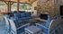 Inviting outdoor lounge area with comfortable blue cushioned seating, a cozy stone fireplace, and a stylish wooden bar setup under a charming wooden pergola.