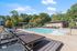 Luxurious outdoor swimming pool area with modern lounge chairs, surrounded by lush green trees and clear blue skies.