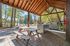Charming outdoor pavilion with rustic wooden picnic table and modern grills, overlooking a serene lake surrounded by lush trees.