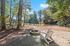 Serene lakeside view with cozy Adirondack chairs, surrounded by lush trees and a picturesque firepit, perfect for relaxation and nature appreciation.