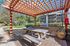 Charming outdoor space showcasing a wooden pergola, rustic picnic table, and modern grill, perfect for leisurely gatherings.