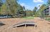 Inviting community park area with manicured green space, shaded seating, and natural wood play equipment, perfect for family enjoyment.