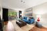 Elegant living room with a stylish blue sofa, modern artwork, and floor-to-ceiling windows opening to a lush balcony view. Perfect blend of comfort and style.