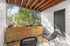 Charming outdoor balcony with woven chairs, vibrant wooden planter, and lush green view, ideal for relaxing and enjoying nature.