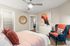 Inviting bedroom with modern decor, featuring a cozy bed with colorful pillows, a stylish blue armchair, and elegant artwork on the wall.
