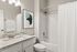 Elegant bathroom featuring a modern vanity with granite countertop, stylish artwork, and a pristine shower area with white tiles.