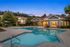 Inviting apartment complex with a luxurious swimming pool, surrounded by lush greenery and elegant architecture at sunset.