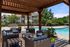 Inviting outdoor lounge area featuring modern wicker furniture under a wooden pergola, overlooking a sparkling swimming pool with lush landscaping.