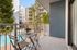 Charming balcony view from a modern apartment overlooking a sunlit swimming pool and lush greenery.