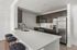 Modern kitchen with sleek dark cabinetry, stainless steel appliances, and a spacious white countertop with stylish bar stools.