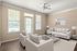 Elegant living room with modern decor, featuring cozy beige seating, a glass coffee table, large windows for ample natural light, and stylish wall art.