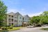 Charming apartment complex surrounded by lush greenery and ample parking space under a bright blue sky.