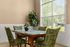 Charming dining area with a sleek wooden table, green patterned chairs, and large sunlit window offering a garden view.