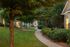 Charming residential pathway surrounded by lush greenery and well-maintained gardens, leading to inviting homes with warm lighting.