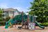 Charming apartment complex with a colorful playground, ideal for families, surrounded by lush green trees.