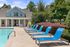 Luxurious outdoor pool area featuring sleek blue lounge chairs and a charming clubhouse, surrounded by lush greenery.