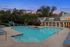 Luxurious apartment complex with inviting pool, modern lounge chairs, and charming clubhouse surrounded by lush greenery, set against a picturesque sunset.