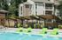 Modern apartment community with a refreshing pool and stylish green lounge chairs under sleek wooden cabanas, surrounded by lush landscaping.