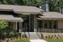 Modern home exterior with sleek stone facade and inviting entrance surrounded by lush greenery.