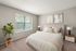 Inviting bedroom with a cozy bed, soft beige decor, modern side tables, and a calming view of lush greenery through a large window.