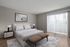 Bright and modern bedroom with a cozy bed, abstract wall art, and large window with stylish blinds.