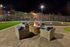 Inviting outdoor space with cozy wicker seating around a glowing fire pit, adjacent to a well-lit sports court, perfect for evenings under the stars.