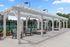 Charming outdoor seating area featuring a modern white pergola, comfortable cushioned chairs, and a lush green backdrop.