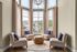 Elegant apartment living space featuring a bright corner with large windows, plush chairs, and chic decor, offering a serene view.