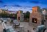 Chic outdoor patio featuring cozy stone fireplaces, stylish seating, and ambient string lights against a twilight sky.