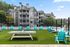 Luxurious apartment complex featuring a vibrant outdoor recreation area with a ping pong table, seating, and a sports court, surrounded by lush greenery.