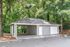 Charming covered parking area surrounded by lush greenery, featuring a modern grey exterior and white doors.