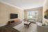 Elegant living room with sleek hardwood floors, large windows illuminating the space, modern TV setup, and cozy beige sofas accented with plush pillows.