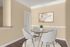 Elegant dining area with modern glass table, plush white chairs, a chic art piece, and warm beige walls, creating an inviting atmosphere.