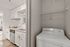 Modern kitchen with sleek white cabinets, stainless steel dishwasher, and cozy adjacent laundry area in bright open apartment.