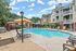 Inviting apartment complex with a sparkling outdoor pool, sunlit lounge chairs, and vibrant orange umbrellas for a perfect relaxation retreat.