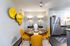 Chic dining area with vibrant yellow chairs and modern decor, next to a sleek stainless steel kitchen in a stylish apartment.