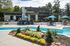 Luxurious apartment complex with a modern poolside, elegant outdoor seating, and vibrant landscaping under a clear sky.