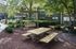 Charming outdoor area featuring a wooden picnic table and a cozy swing bench under the shade of lush green trees, perfect for relaxation and gatherings.