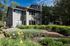 Charming townhouse with modern gray exterior surrounded by lush greenery and beautiful landscaping on a sunny day.