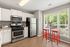 Bright, modern kitchen with white cabinets, stainless steel appliances, and a cozy seating area with vibrant red stools by a large window.