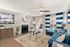 Modern living room with stylish decor, featuring a cozy fireplace, vibrant blue sectional sofa, chic artwork, and a large window with striped curtains inviting natural light.