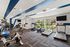 Modern fitness center with state-of-the-art equipment, large windows overlooking lush greenery, and vibrant blue architectural accents.