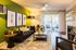 Vibrant living room with stylish decor, featuring a bold green accent wall, contemporary artwork, and a cozy seating area opening to a serene balcony view.