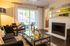 Inviting living room with elegant decor, featuring a cozy fireplace, sleek glass table, and bright natural light from large windows overlooking a tranquil balcony.