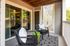 Charming balcony with cozy black wicker chairs, decorative cushions, and a stylish geometric rug, perfect for relaxing and enjoying the greenery view.